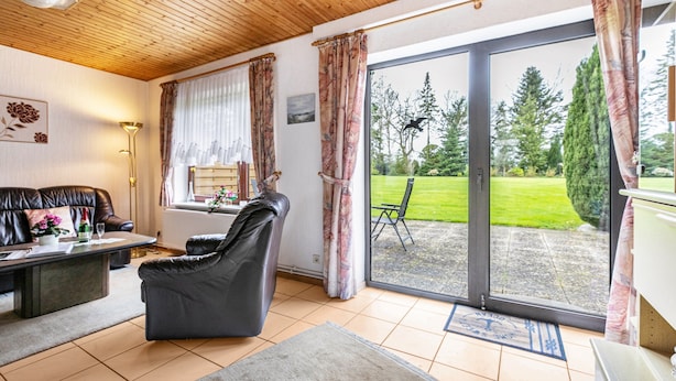 A living room with a sofa, a chair, a coffee table, and a view of a garden through a sliding glass door.