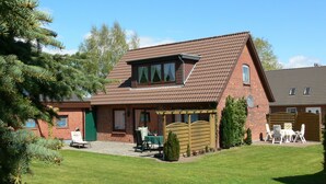 A brick house with a sloped roof, a front porch with a table and chairs, and a well-maintained lawn.