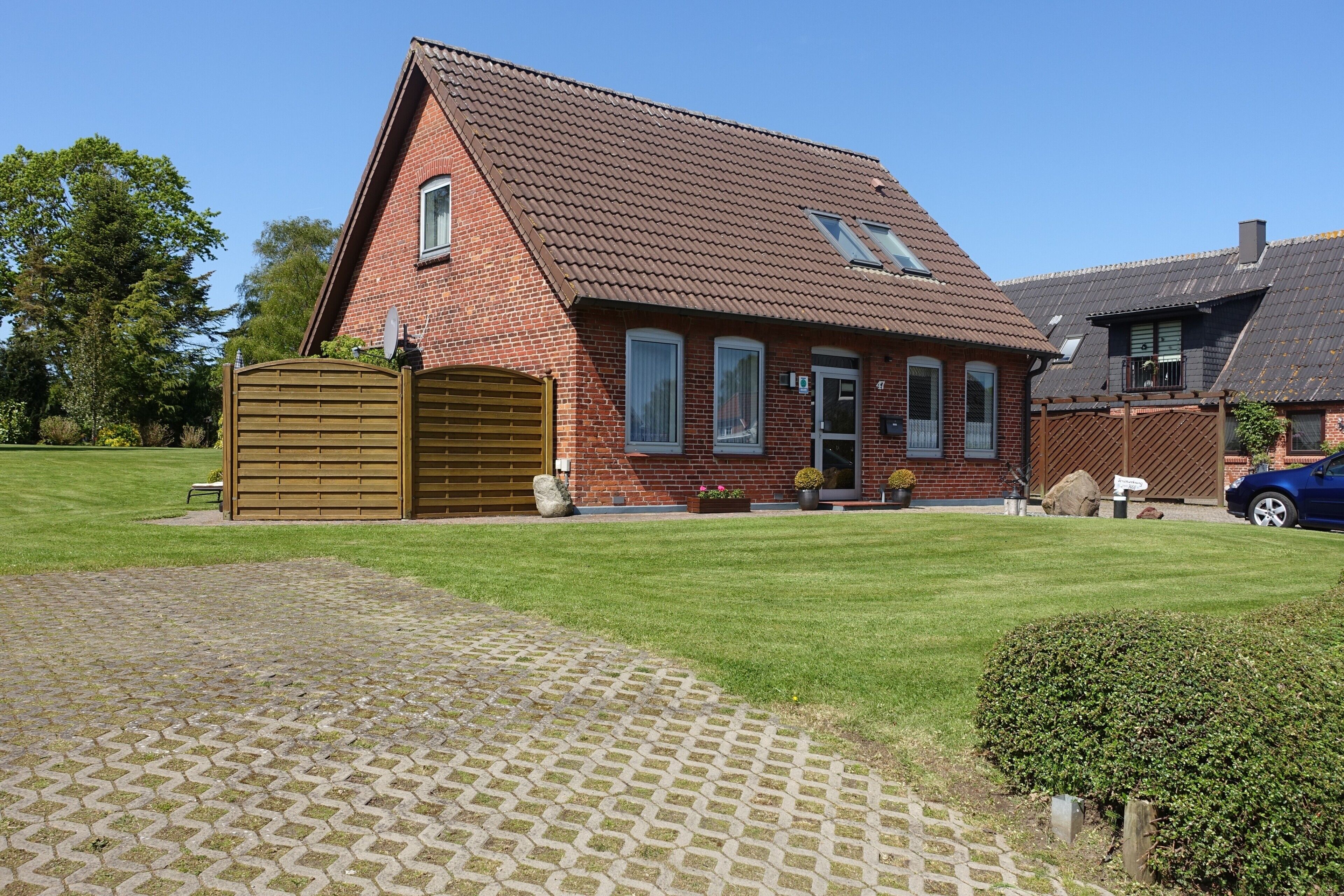 A brick house with a sloped roof, a wooden gate, and a paved driveway.