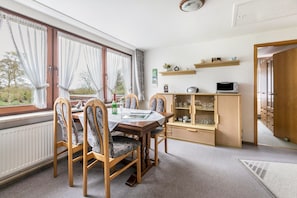 A dining area with a table, chairs, a cabinet with glassware, and a window with curtains. - Holiday Apartment 'Ferienhaus Christa - Falshöft' with Private Terrace and Garden (Rabel)