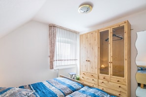 A bedroom with a bed, a wardrobe, a window with curtains, and a radiator. - Holiday Apartment 'Ferienhaus Christa - Falshöft' with Private Terrace and Garden (Rabel)