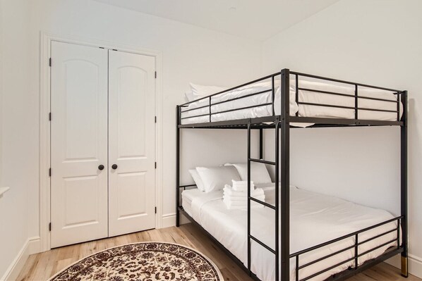 Una cama individual con ropa blanca, una puerta blanca y una alfombra estampada.