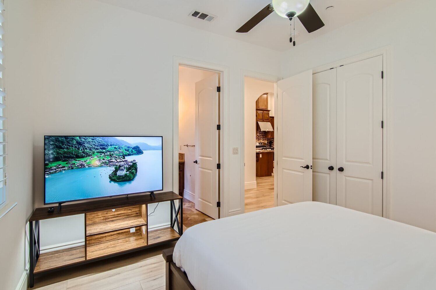 A bedroom with a bed, a TV on a wooden stand, and a ceiling fan.