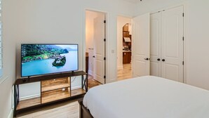 Een slaapkamer met een bed, een televisie op een houten standaard en een plafondventilator.