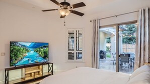 Een slaapkamer met een groot bed, een televisie op een houten dressoir, een plafondventilator en een schuifdeur naar een buitenpatio met een tafel en stoelen.