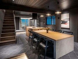 Una cocina moderna con una isla central, baldosas oscuras y una escalera de madera.