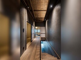 Un interior moderno con escalera de madera, paredes oscuras y techo con vigas a la vista.