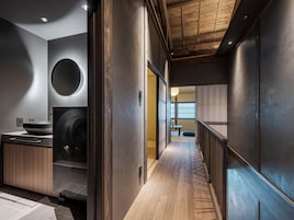 Un interior moderno con techo de madera, una zona de cocina con pileta y lavadora, y un pasillo que lleva a una habitación con ventana.