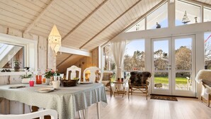 Ein gemütlicher Essbereich mit Holztisch, weißen Stühlen und Blick ins Freie durch große Fenster.