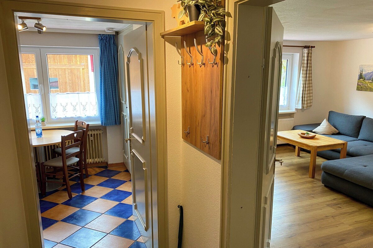 A living room with a sofa, a dining table with chairs, and a kitchen area with a radiator.