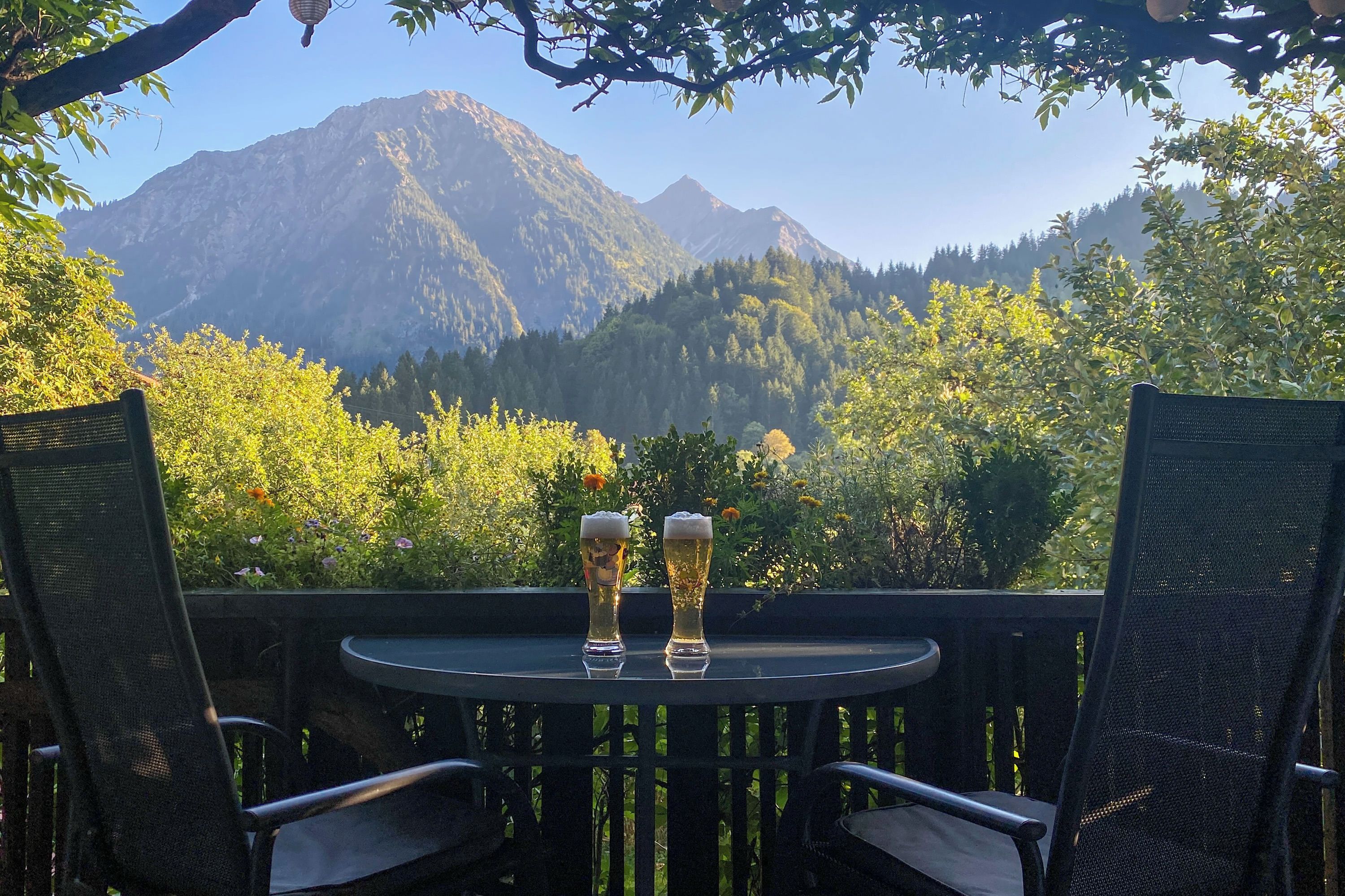 Ein Tisch mit zwei Biergläsern, umgeben von Stühlen, mit Blick auf eine gebirgige Landschaft.