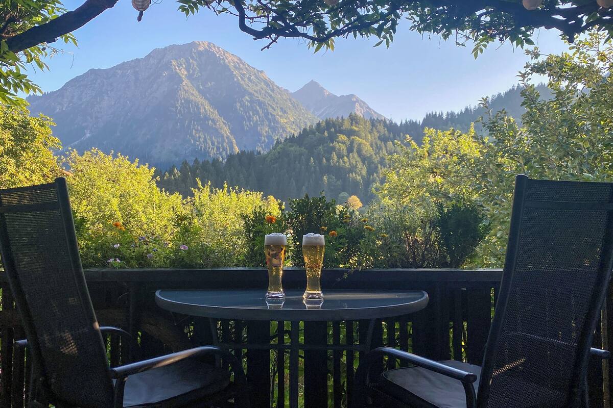 A table with two glasses of beer and two chairs, overlooking a mountainous landscape.