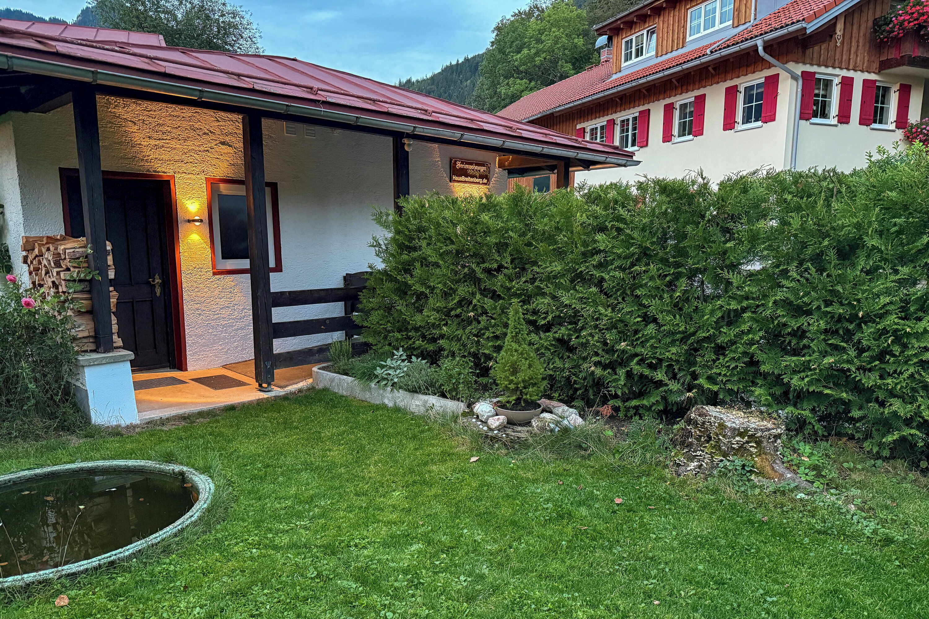 A traditional chalet with a wooden facade, a stone entrance, and a well-maintained garden with a pond.