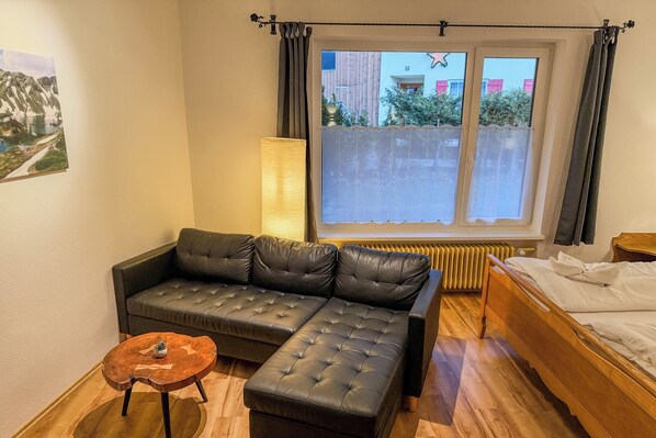 Una habitación moderna con un sofá de cuero, una mesita de madera, una cama y un ventanal con cortinas.