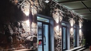 Comedor con pared de piedra rústica, ventanas amplias y mesa de madera con sillas.