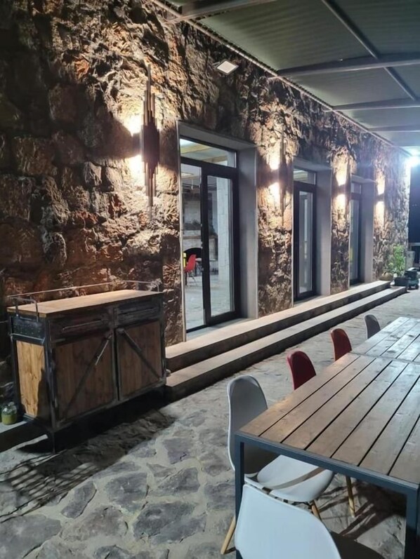 Un espacio de estar al aire libre de estilo rústico, con paredes de piedra, una mesa de madera y sillas.
