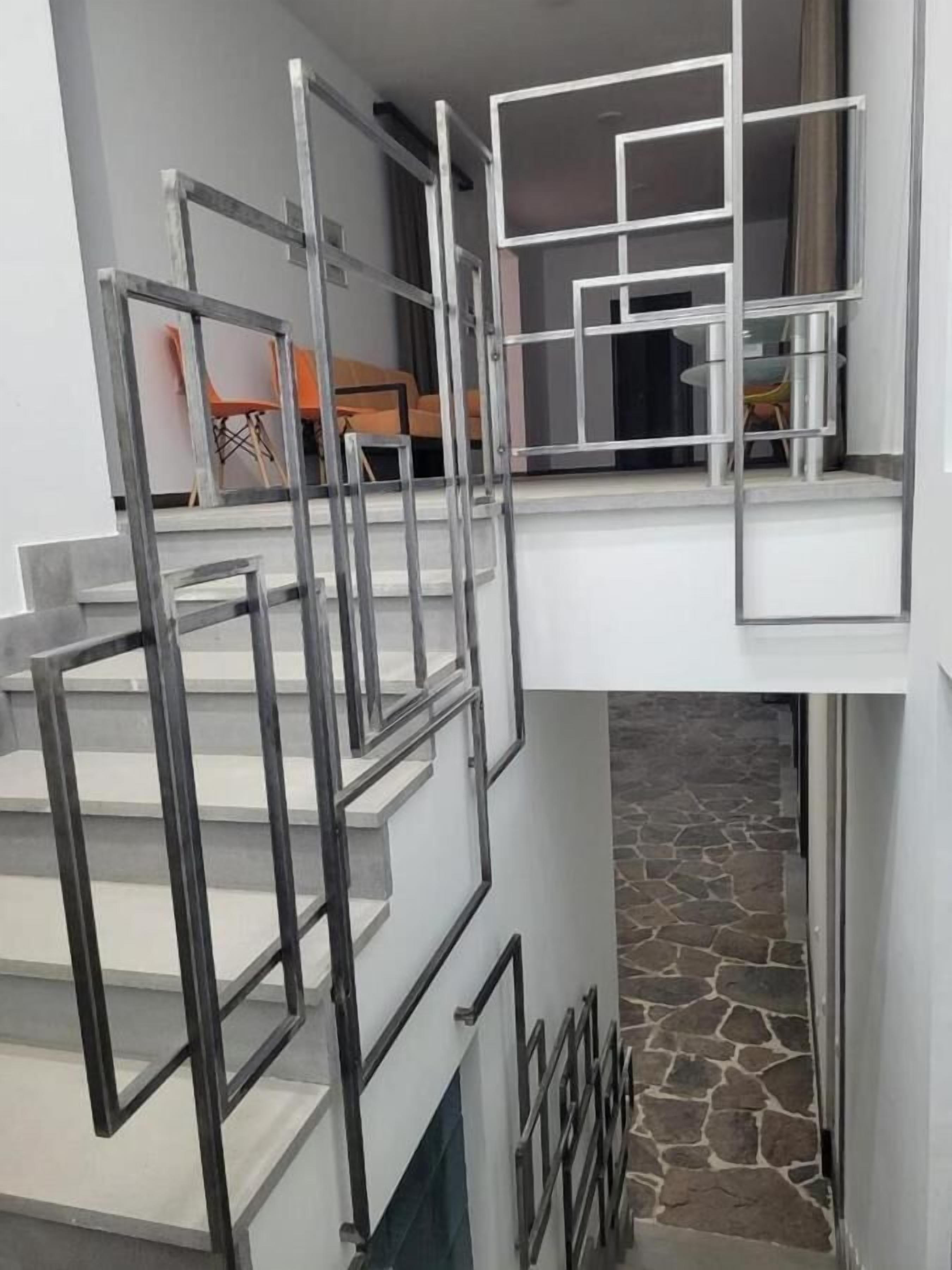 Μια σύγχρονη σκάλα με μεταλλικά κάγκελα και δάπεδο επενδεδυμένο με πέτρα, η οποία οδηγεί σε έναν χώρο στον δεύτερο όροφο, όπου υπάρχουν ένα τραπέζι και καρέκλες από γυαλί.