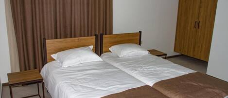 A double bed with white bedding and a brown throw blanket, two bedside tables, and a wooden wardrobe in a hotel room.