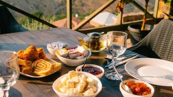A table set with various food items and a glass of wine, overlooking a mountainous landscape.