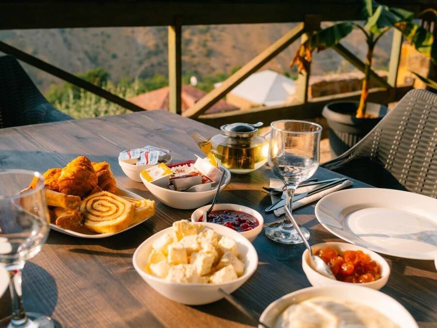 A table set with various food items and a glass of wine, overlooking a mountainous landscape.