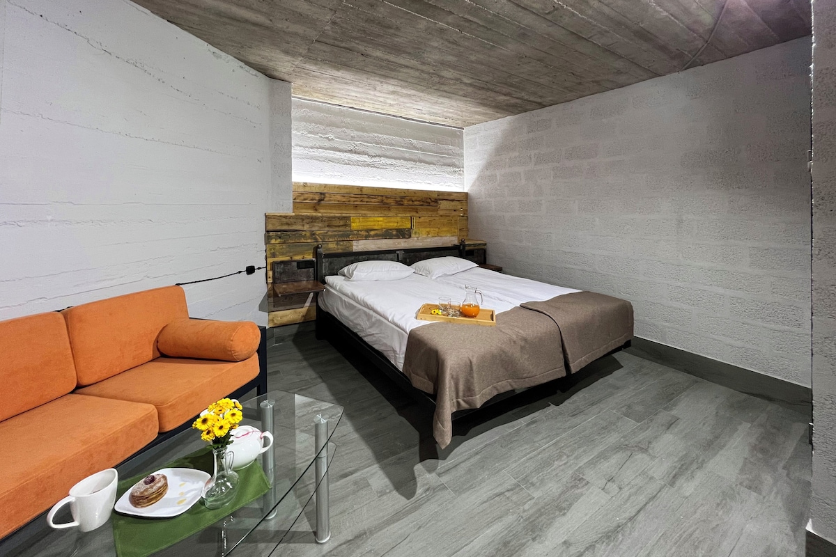 A bedroom with a bed, a nightstand, a glass table with a cup, a plate with food, and a vase with flowers.