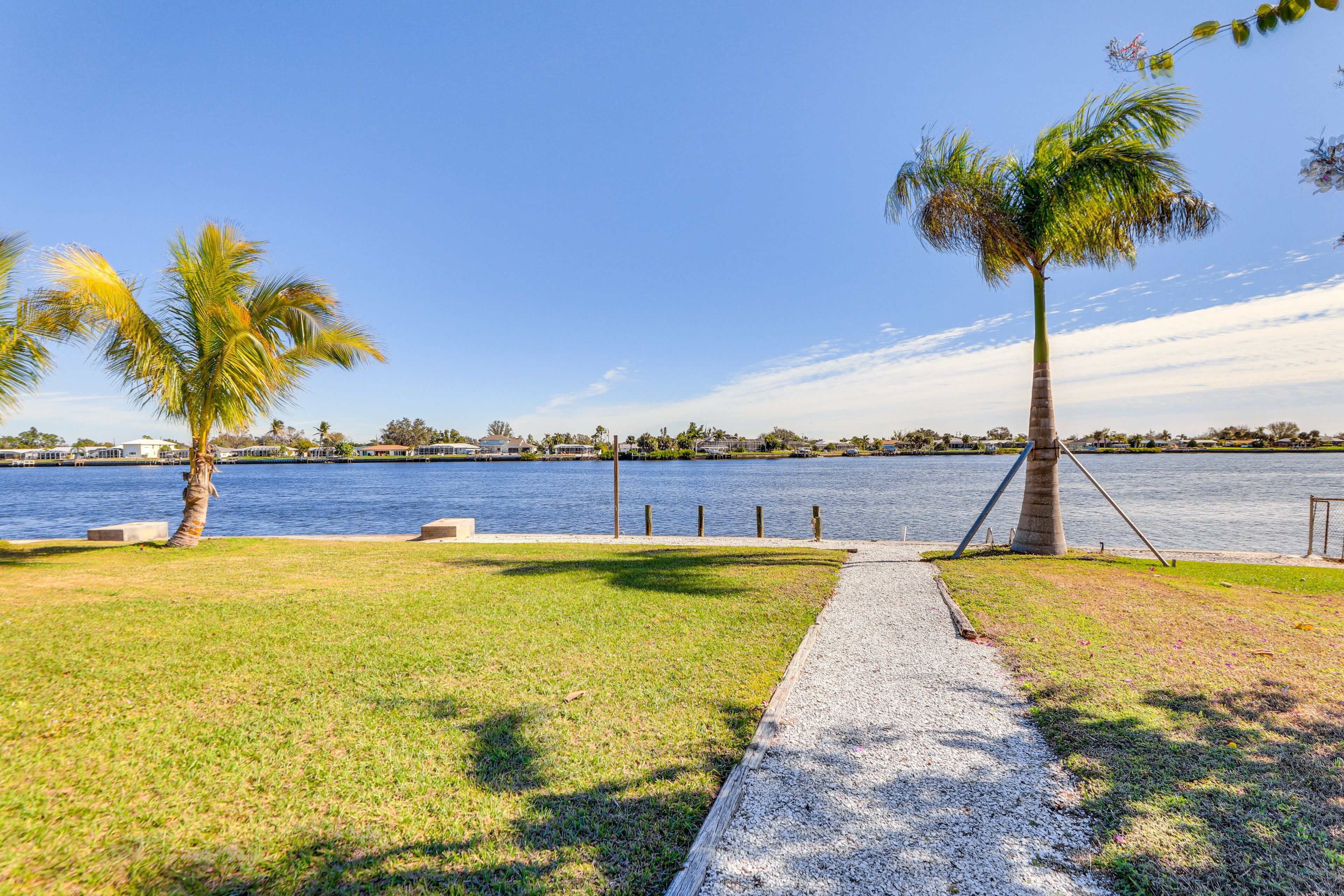 A waterfront park with a pathway, palm trees, and a view of the water.