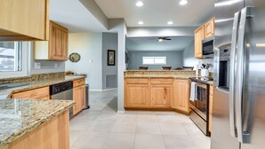 Una cocina moderna con encimeras de granito, armarios de madera y electrodomésticos de acero inoxidable, además de un ventilador de techo.