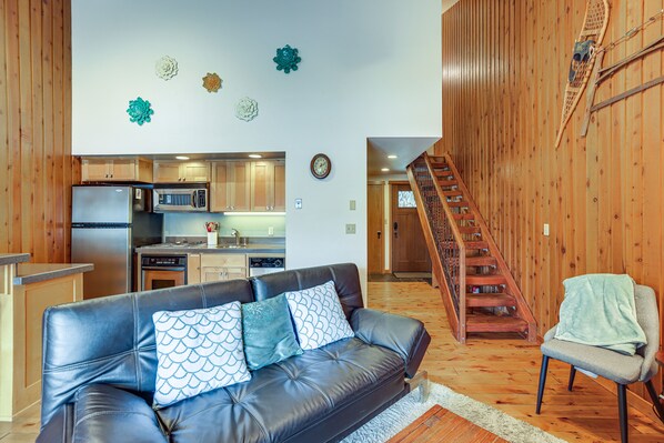 Una sala de estar con un sofá de cuero, una escalera y una cocina al fondo.