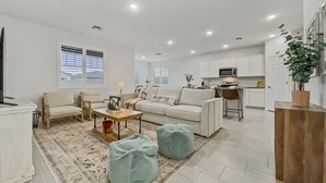 A modern living room with a sofa, two armchairs, a coffee table, and a rug. There is a kitchen area in the background with white cabinets and a microwave. - 3BR w playroom, community pool/spa! (Queen Creek)