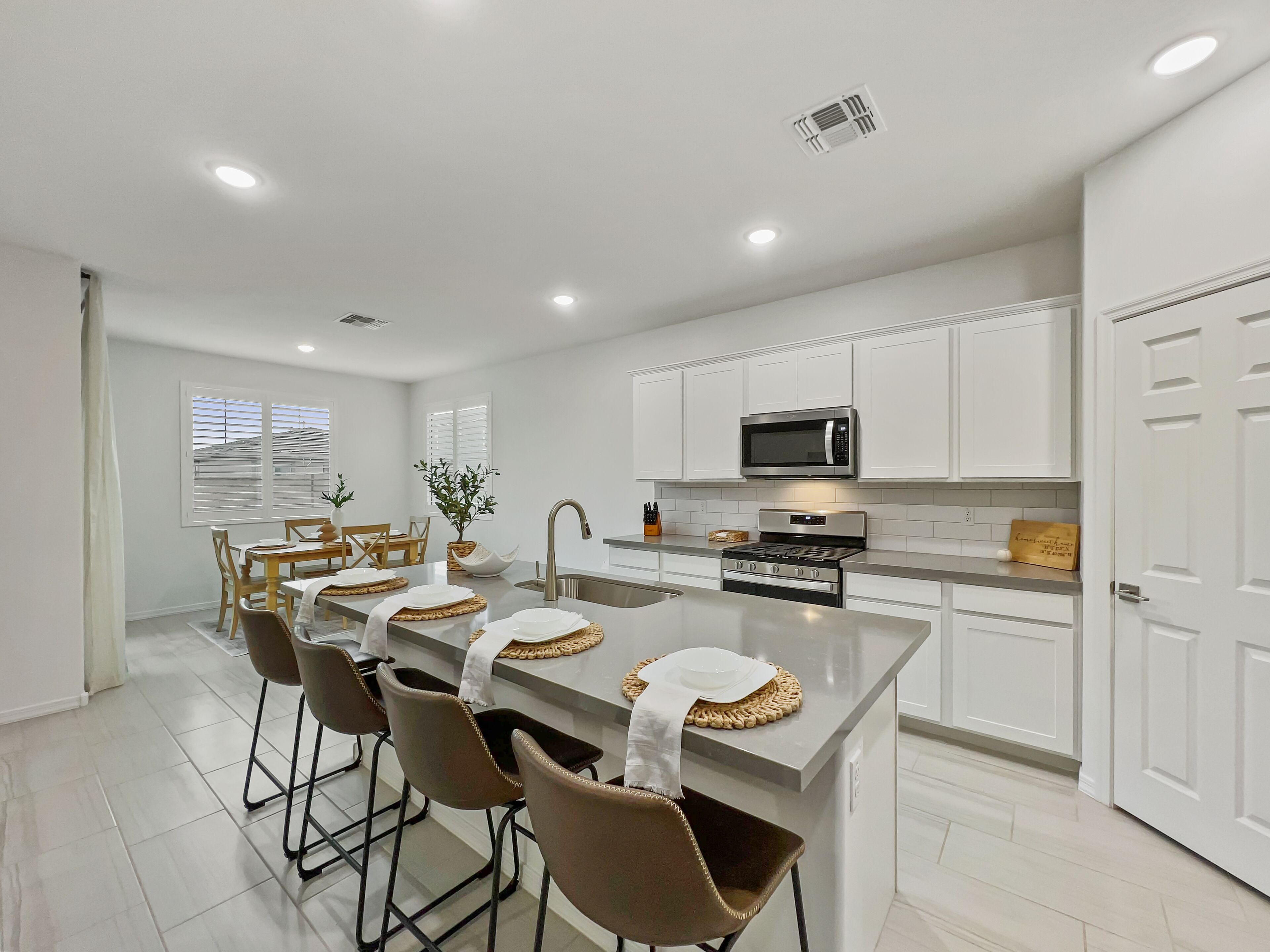 A modern kitchen with white cabinetry, a central island with bar stools, a stainless steel microwave, and a built-in oven.