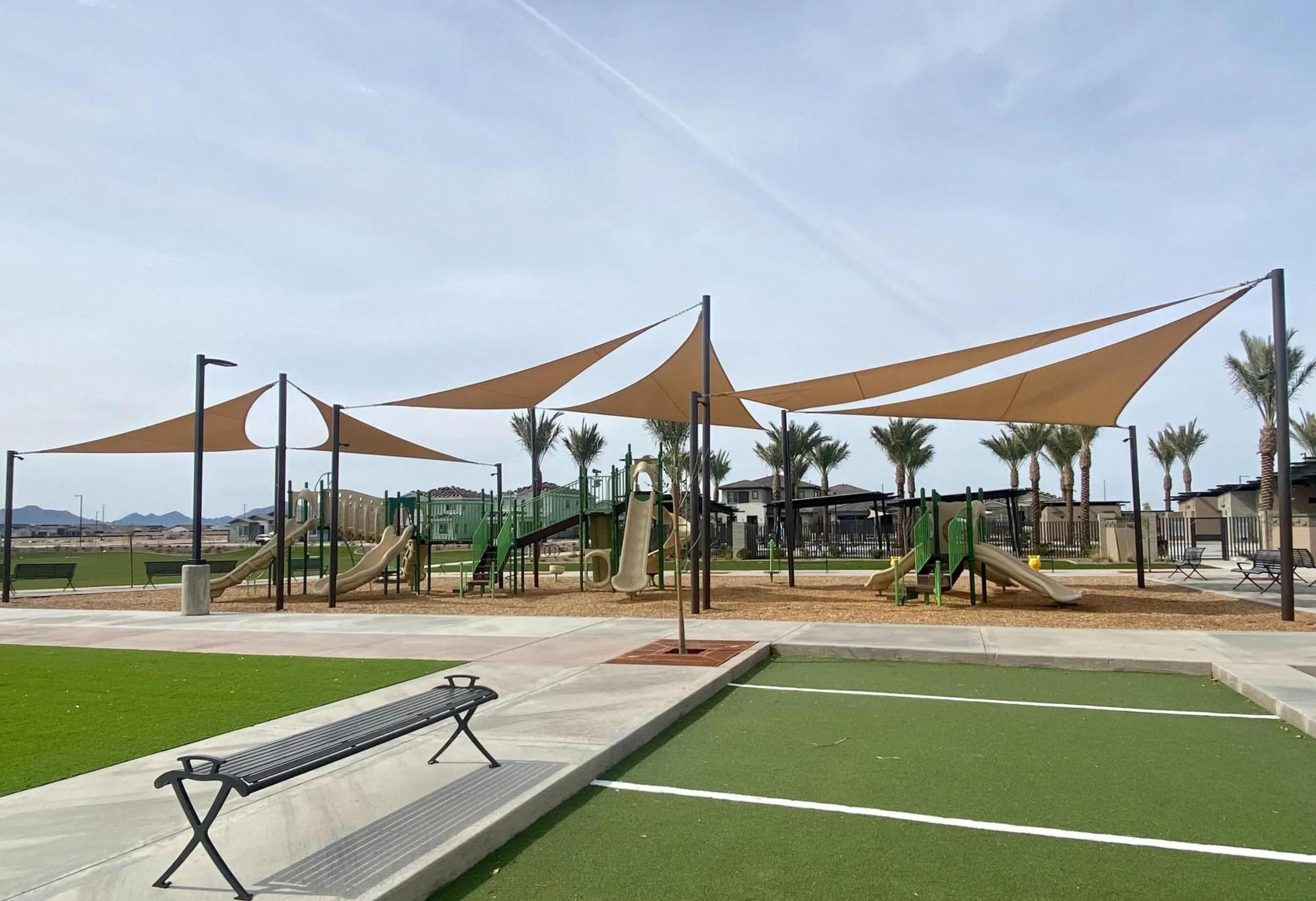 A playground with slides and climbing structures, surrounded by palm trees and benches.