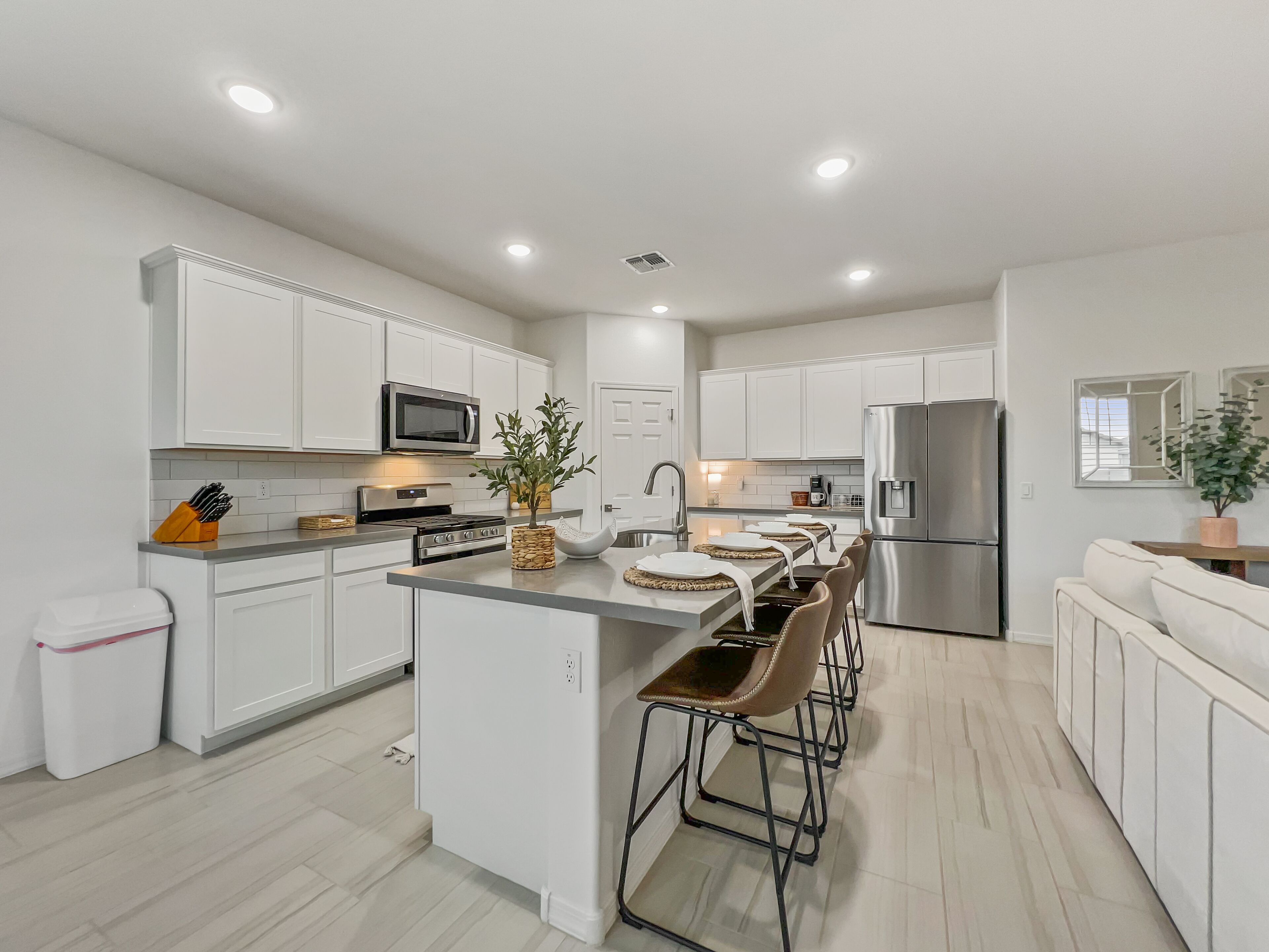 Una cocina moderna con armarios blancos, electrodomésticos de acero inoxidable y una isla central con taburetes de bar.