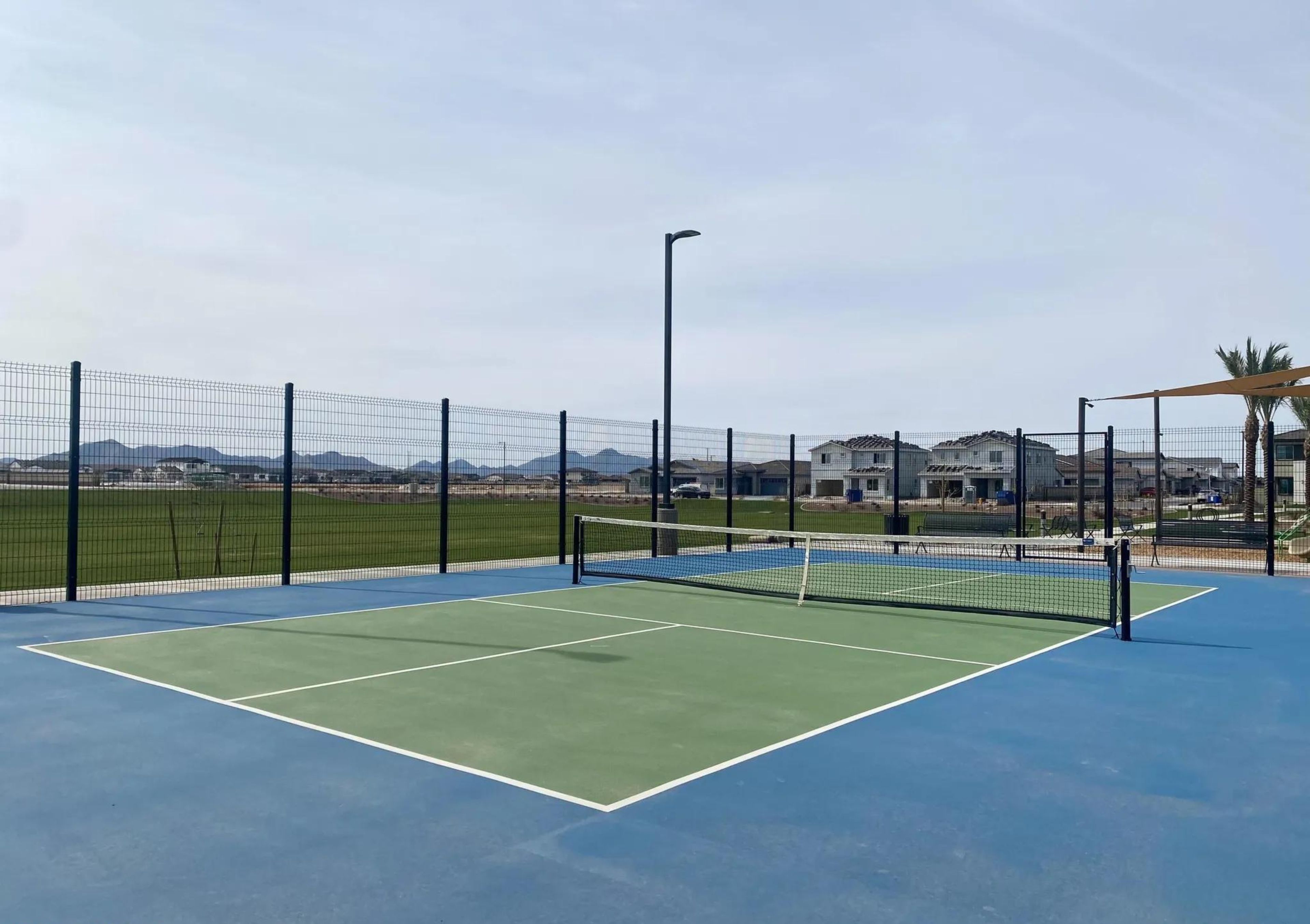 Een tennisbaan buiten met een net, omgeven door een hek, en een heldere lucht.