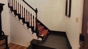 Un escalier avec une main courante noire et des balustrades blanches, menant à un palier agrémenté d’un lustre.