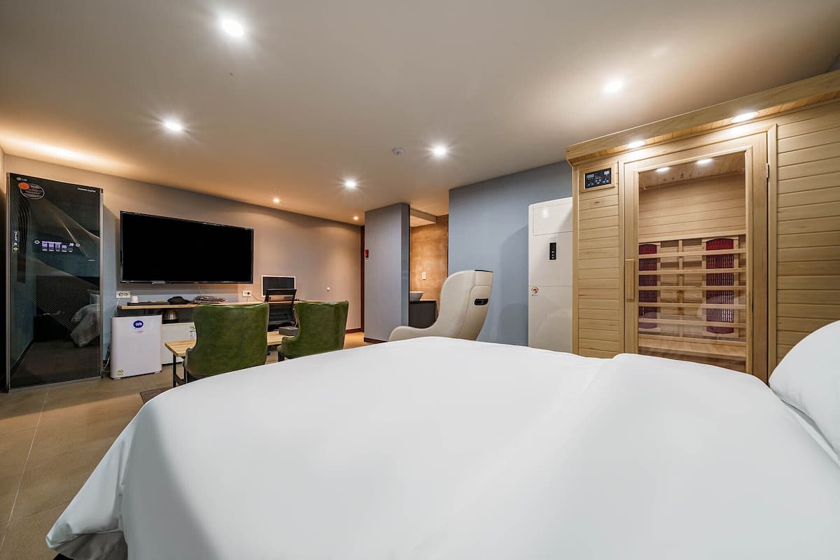 A modern hotel room with a large bed, a desk with a computer, a television, and a sauna.