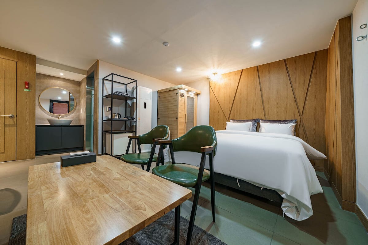 A modern hotel room with a wooden floor, a round mirror, a bed with white linens, a small table, and two chairs.