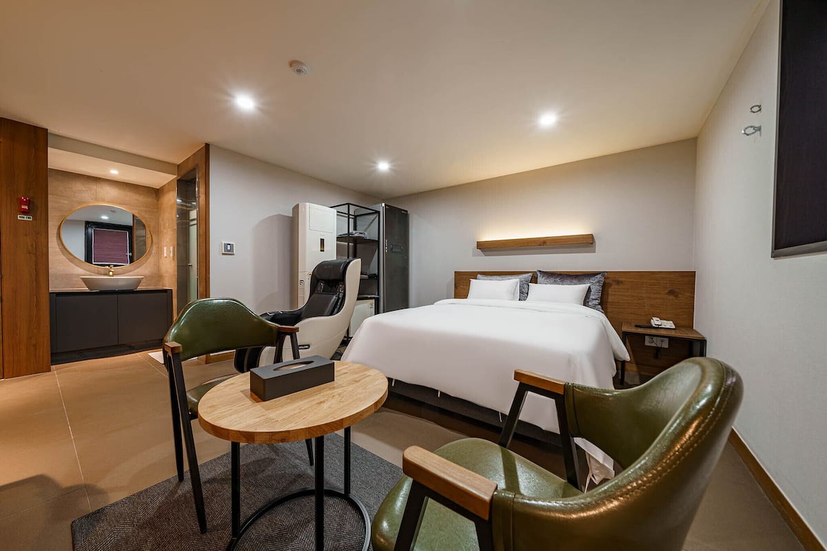 A hotel room with a bed, a desk, two chairs, a small table, a mirror, a wardrobe, and a nightstand.
