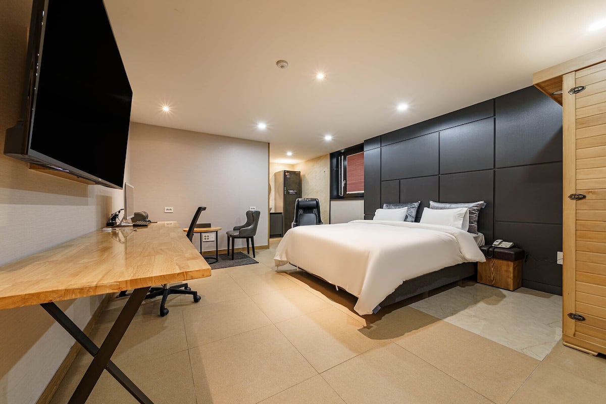 A modern hotel room with a large bed, a desk with a chair, a flat-screen TV, and a wooden door.