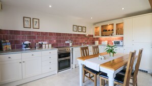 A modern kitchen with white cabinets, a wooden dining table, and a red-tiled backsplash. - Woodland View (Barnstaple)