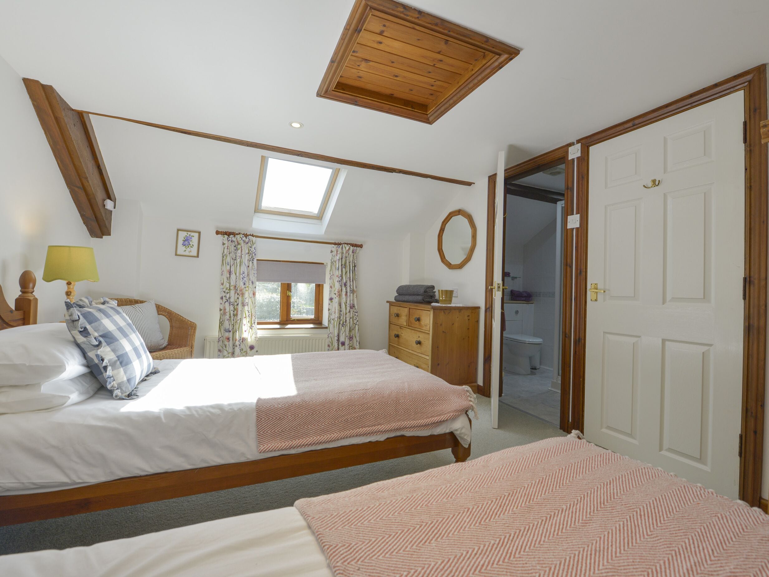 Une chambre avec deux lits, une lucarne, une commode en bois et une salle de bain visible à travers une porte ouverte.