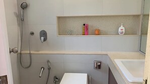 A bathroom with a shower, toilet, sink, and a shelf with toiletries.