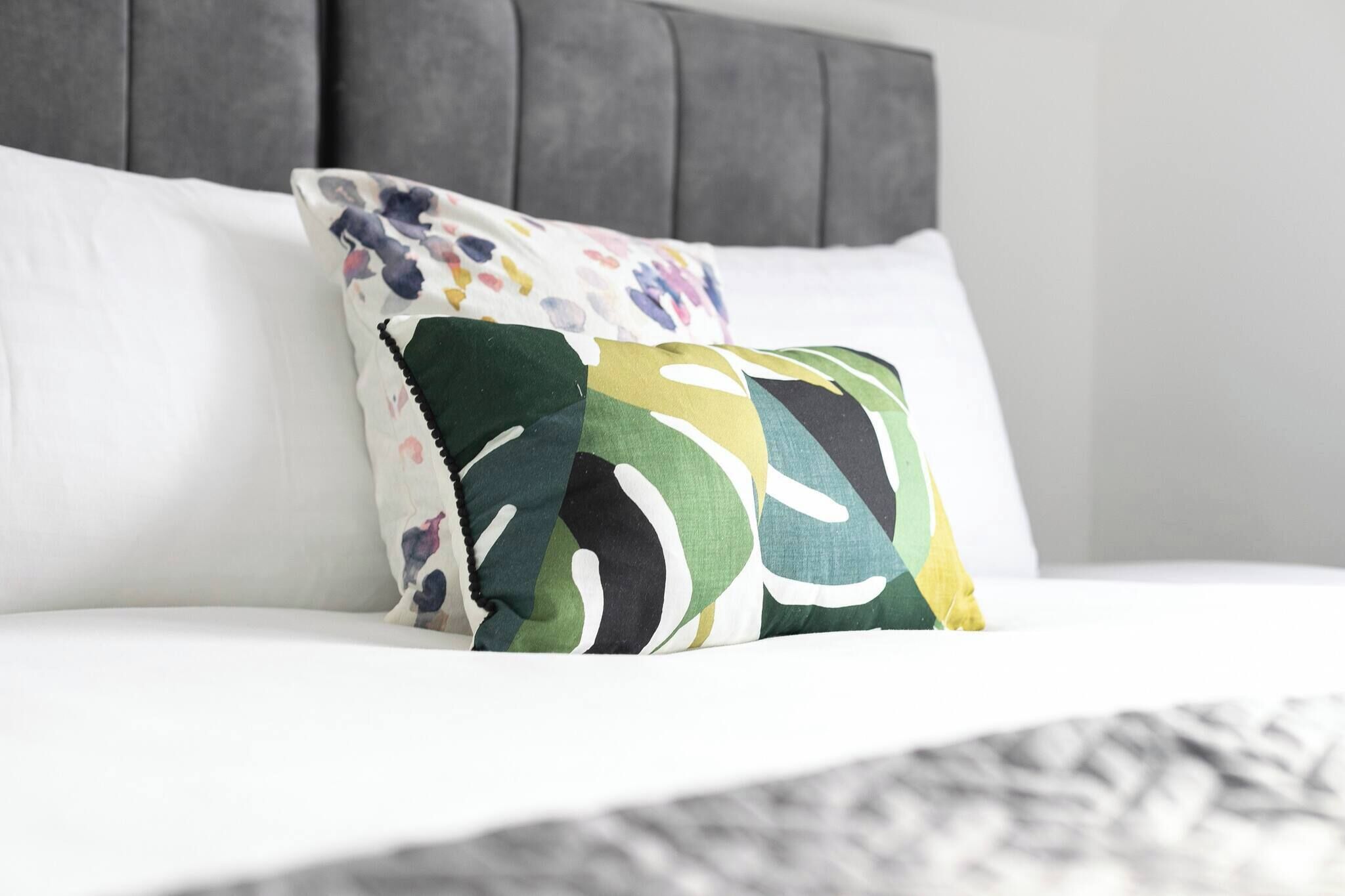 A bed with white bedding and two pillows, one with a floral pattern and the other with abstract designs.