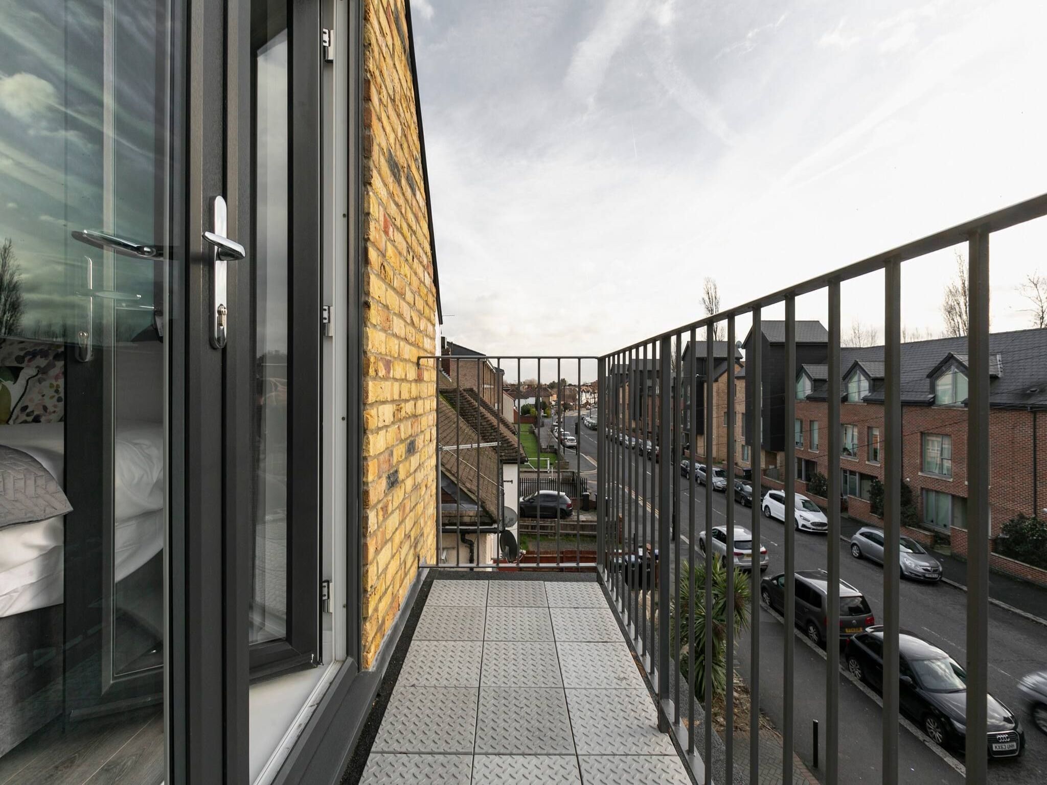 A balcony with a view of a residential street, a brick wall, and a metal railing.