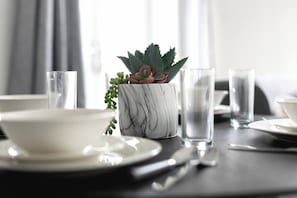 Une table à manger avec un bol blanc, un verre et un pot en marbre contenant une plante succulente.