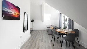 A modern dining area with a round table, chairs, and a sofa in a bright room with a sloped ceiling. - Skyvillion -vineyard Court Enfield 1bed Wbalcony (Enfield)