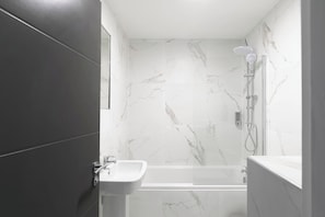 A bathroom with a shower, a sink, and marble walls.