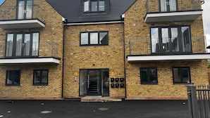 A multi-story brick building with balconies, a central entrance, and a gated driveway. - Skyvillion -vineyard Court Enfield 1bed Wbalcony (Enfield)