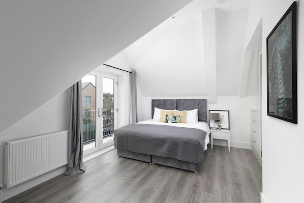 A bedroom with a sloped ceiling, a large bed, a nightstand, a framed picture, and a view through a glass door.