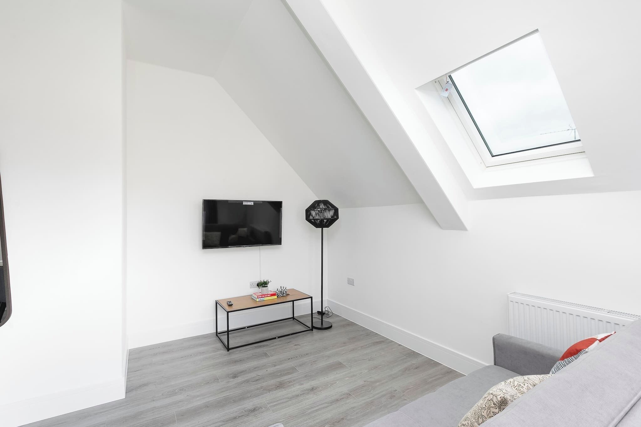 A modern living room with a sloped ceiling, a flat-screen TV, a floor lamp, a small table, and a sofa.