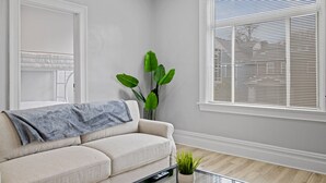 Un salon avec un canapé beige, une petite table sur laquelle est posée une plante, et une fenêtre avec des stores.